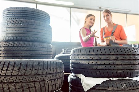 female mechanic - Helpful experienced female auto mechanic checking the identification number of a tire for a customer in an automobile repair shop with various tires for sale Foto de stock - Super Valor sin royalties y Suscripción, Código: 400-09093007
