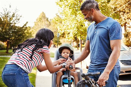 Parents Putting Daughter Into Child Seat For Bike Ride Stock Photo - Budget Royalty-Free & Subscription, Code: 400-09122246