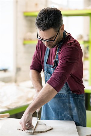 pottery sculpt - Ceramist Dressed in an Apron Cutting the Pieces of Raw Clay in the Bright Ceramic Workshop. Stock Photo - Budget Royalty-Free & Subscription, Code: 400-09132515