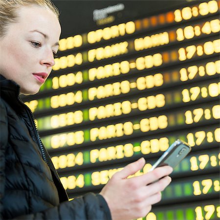 Young woman at international airport looking at the flight information board, holding smart phone in her hand, checking flight informations on phone application. Stock Photo - Budget Royalty-Free & Subscription, Code: 400-09170475