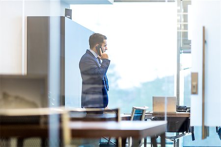 Businessman talking on a mobile phone while looking through modern corporate office window. Stock Photo - Budget Royalty-Free & Subscription, Code: 400-09171332