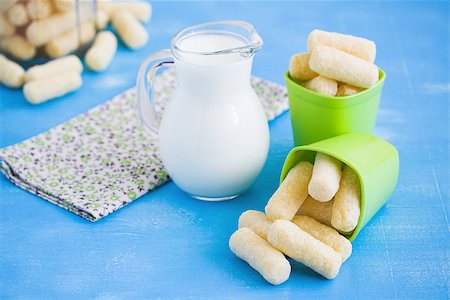 Milk in glass jug and sweet corn sticks with sugar powder in green plastic plates on blue wooden background. Focus  on corn sticks. Stock Photo - Budget Royalty-Free & Subscription, Code: 400-09172194