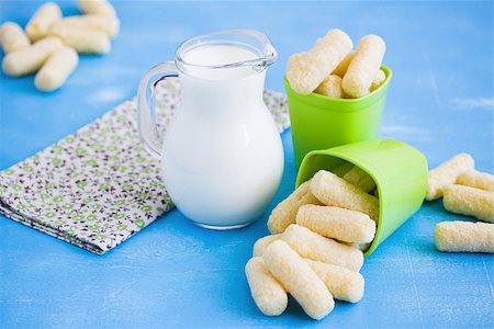 Milk in glass jug and sweet corn sticks with sugar powder in green plastic plates on blue wooden background. Focus  on corn sticks. Stock Photo - Budget Royalty-Free & Subscription, Code: 400-09172193