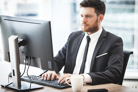 simsearch:400-04283674,k - Young businessman at the office sitting at his desk with hands on keyboard looking at computer screen Foto de stock - Super Valor sin royalties y Suscripción, Código: 400-09225359