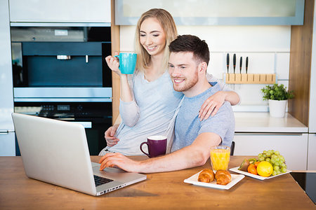 family eating computer - Portrait of a smiling loving couple having breakfast while sitting at the table in a kitchen at home and looking at laptop computer Stock Photo - Budget Royalty-Free & Subscription, Code: 400-09225528