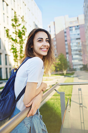 portrait of a young smiling attractive woman in white t-shirt with small city backpack at sunny day on city building background. woman poses in cityscape. Fotografie stock - Microstock e Abbonamento, Codice: 400-09225860