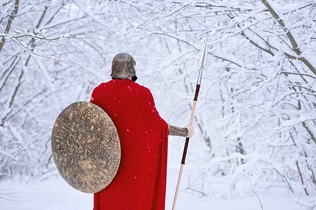 spartan - Careful spartan in cold snowy forest. A man looks brave and strong. He keeps traditional spartan armor: round big shield and sharp metallic spear,helmet on his head. Warrior wears long red cape. Foto de stock - Super Valor sin royalties y Suscripción, Código: 400-09221795