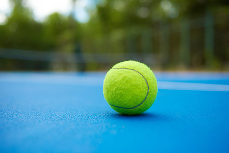 Yellow ball is laying on blue tennis court background. Blurred green plantings and trees behind. Contrast image with satureted colors. Concept of sport equipment photo. Stock Photo - Budget Royalty-Free & Subscription, Code: 400-09221992