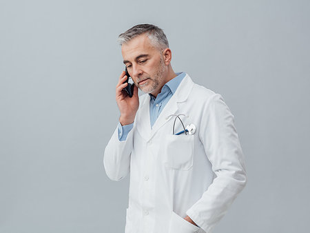simsearch:400-08751444,k - Confident mature doctor having a phone call with his smartphone: medical service consultation by phone Photographie de stock - Aubaine LD & Abonnement, Code: 400-09222951