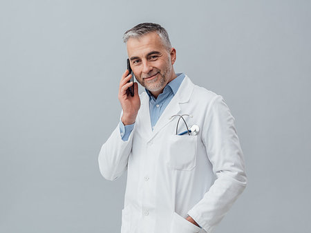 simsearch:400-08751444,k - Confident mature doctor having a phone call with his smartphone: medical service consultation by phone Photographie de stock - Aubaine LD & Abonnement, Code: 400-09222952