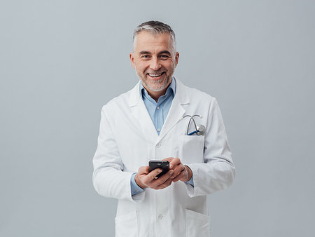 simsearch:400-08751444,k - Smiling mature doctor connecting with his smartphone and doing a medical consultation online Photographie de stock - Aubaine LD & Abonnement, Code: 400-09222953