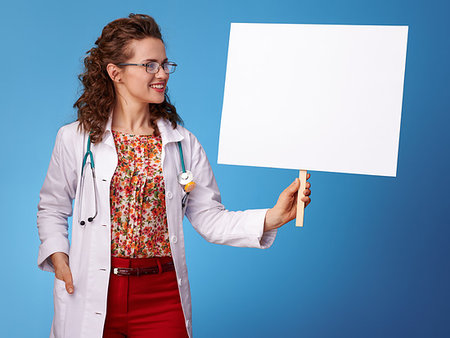 simsearch:400-05745246,k - smiling paediatrician woman in white medical robe looking at placard against blue background Photographie de stock - Aubaine LD & Abonnement, Code: 400-09237717