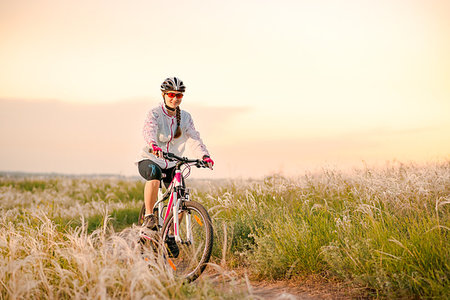 simsearch:400-06922980,k - Young Woman Riding the Mountain Bikes in the Beautiful Field Full of Feather Grass at Sunset. Adventure and Travel Concept. Stock Photo - Budget Royalty-Free & Subscription, Code: 400-09237996