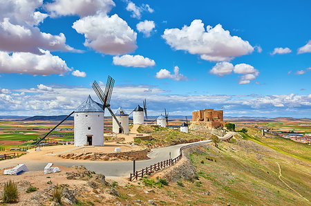 Wind mills and old castle in Consuegra, Toledo, Castilla La Mancha, Spain. Picturesque panorama landscape with road and view to ancient walls and windmills on blue sky with clouds. Stockbilder - Microstock & Abonnement, Bildnummer: 400-09238014