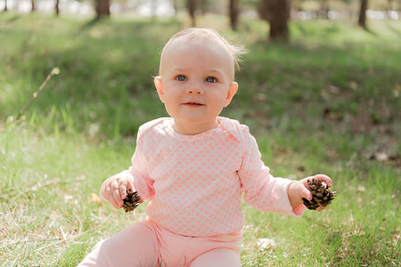 simsearch:400-05248187,k - the baby sits on the grass and plays with two fir cones, she is dressed in a pink blouse against the green grass Photographie de stock - Aubaine LD & Abonnement, Code: 400-09274181
