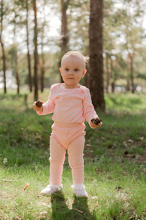 simsearch:400-05248187,k - the baby holds two cones in the spruce forest against the green grass in a pink suit and looks past the camera Photographie de stock - Aubaine LD & Abonnement, Code: 400-09274182