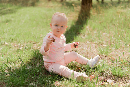 simsearch:400-05248187,k - the baby sits on the grass and plays with two fir cones, she is dressed in a pink blouse against the green grass Photographie de stock - Aubaine LD & Abonnement, Code: 400-09274183