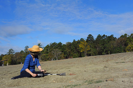 Woman, wearing a straw hat and holding a trowel, digs in the dirt at Crater of Diamonds State Park in Murfreesboro, Arkansas.  She is all alone in the field. Fotografie stock - Microstock e Abbonamento, Codice: 400-09274594