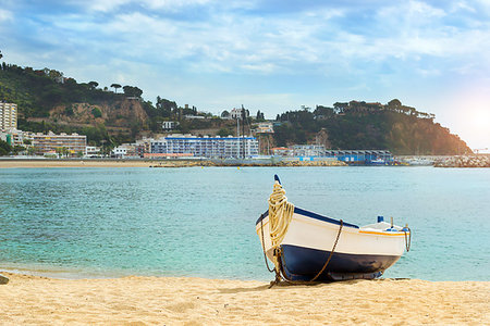 simsearch:851-02963102,k - Fishing boat moored on the sandy beach on the background of the seaport. Coast of sandy beach and architecture of Spanish beach resort Blanes in summertime. Costa Brava, Catalonia, Spain Stock Photo - Budget Royalty-Free & Subscription, Code: 400-09274609