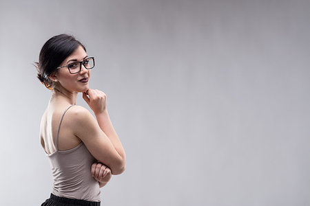 simsearch:6109-08690493,k - Beautiful young brunette woman with dark lipstick, wearing grey top and large glasses, standing against grey background with copy space and looking at camera over her bare shoulder Stockbilder - Microstock & Abonnement, Bildnummer: 400-09273464