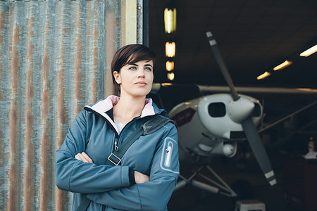 female old aviator - Smiling young woman leaning against the hangar metallic rusty walls, light aircraft on the background Stock Photo - Budget Royalty-Free & Subscription, Code: 400-09273859