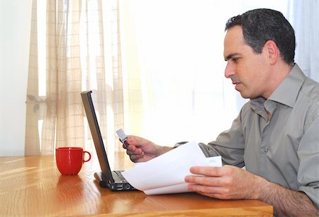 simsearch:400-04130596,k - Man sitting at his desk with laptop, papers and credit card Stock Photo - Budget Royalty-Free & Subscription, Code: 400-03915228