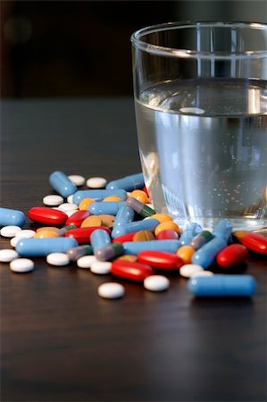 simsearch:400-05002215,k - Collection of assorted pills beside a glass of water on a dark wood table. Shallow depth-of-field. Photographie de stock - Aubaine LD & Abonnement, Code: 400-03915405