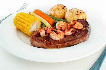 Meal setting of a steak with garlic butter sauce and fresh king prawns - surf n' turf - and fresh vegetables, on a white plate with knife and fork isolated on white Stock Photo - Budget Royalty-Free & Subscription, Code: 400-03911600