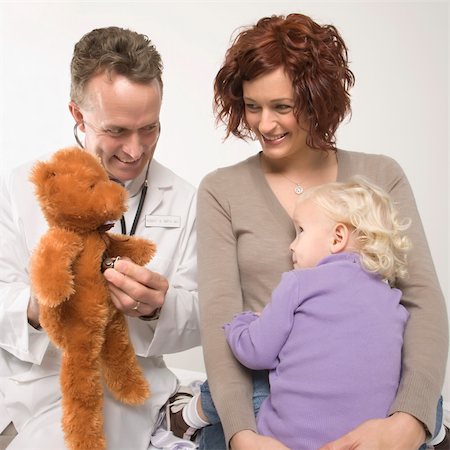 Middle-aged adult Caucasian male doctor holding stethoscope to teddy bear while Caucasian mother and daughter watch. Stock Photo - Budget Royalty-Free & Subscription, Code: 400-03924174