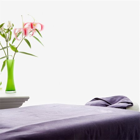 simsearch:400-04956215,k - Spa scene of massage table with purple sheets and table with pink Easter lillies in green vase. Photographie de stock - Aubaine LD & Abonnement, Code: 400-03925689