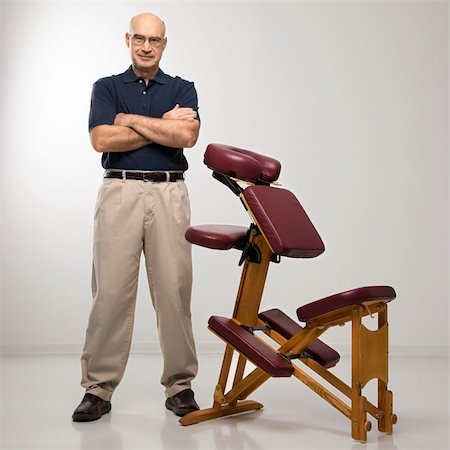 simsearch:400-04956215,k - Caucasian middle-aged male massage therapist standing with arms crossed beside massage chair. Photographie de stock - Aubaine LD & Abonnement, Code: 400-03925682