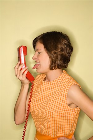 Pretty Caucasian mid-adult woman wearing orange dress sticking out tongue at red telephone receiver. Stock Photo - Budget Royalty-Free & Subscription, Code: 400-03925714