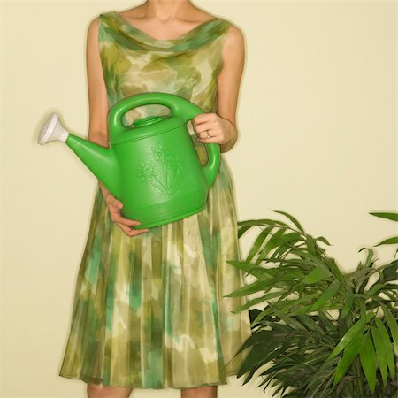 simsearch:400-04451365,k - Pretty Caucasian mid-adult woman wearing vintage dress standing next to houseplant holding green watering can. Foto de stock - Super Valor sin royalties y Suscripción, Código: 400-03925736