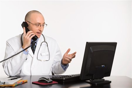 simsearch:400-03924532,k - Caucasian mid adult male physician sitting at desk with laptop computer talking on telephone. Stock Photo - Budget Royalty-Free & Subscription, Code: 400-03926375