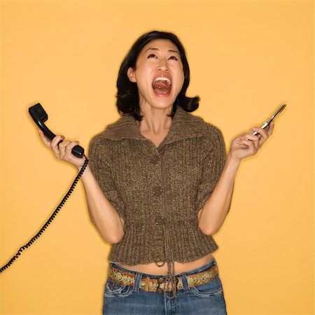 simsearch:400-03925541,k - Pretty mid adult Asian woman holding telephone and cellphone with mouth open. Foto de stock - Super Valor sin royalties y Suscripción, Código: 400-03926406