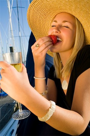 A stunningly beautiful and wealthy young blond woman sitting on the deck of her yacht in a marina eating strawberries and drinking champagne Stock Photo - Budget Royalty-Free & Subscription, Code: 400-03927081