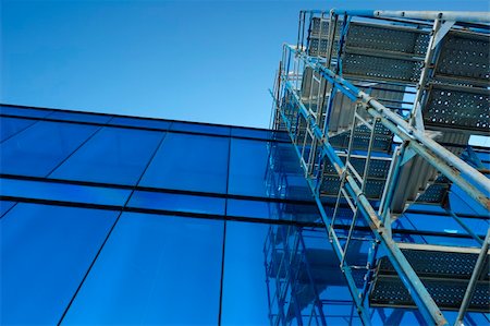 simsearch:400-03938926,k - A tower of scaffolding, angular and open, contrasts with the smooth mirror-like facade of an office building Photographie de stock - Aubaine LD & Abonnement, Code: 400-03921084