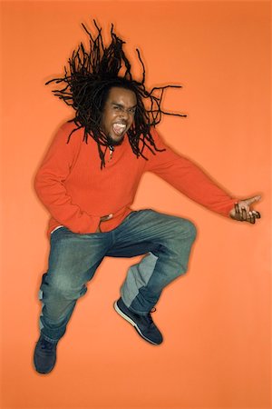 rastafarian - African-American mid-adult man on orange background jumping while playing air guitar. Stock Photo - Budget Royalty-Free & Subscription, Code: 400-03921117