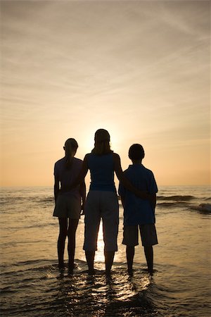 simsearch:400-03923118,k - Caucasian mid-adult mother and teenage kids standing silhouetted on beach at sunset. Fotografie stock - Microstock e Abbonamento, Codice: 400-03923423