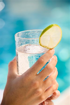simsearch:700-01042205,k - Caucasian woman's hands holding drink glass garnished with lime slice next to pool. Foto de stock - Royalty-Free Super Valor e Assinatura, Número: 400-03937636