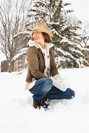 pelea de bolas de nieve - Caucasian young adult female looking over shoulder while kneeling in snow with snowball and wearing straw cowboy hat. Foto de stock - Super Valor sin royalties y Suscripción, Código: 400-03937671