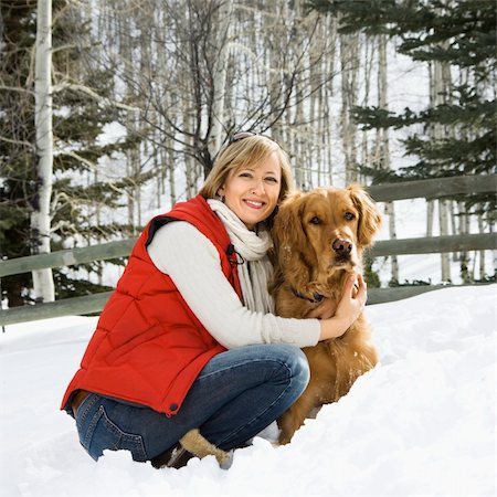 simsearch:400-03944669,k - Attractive smiling mid adult Caucasian blond woman squatting in snow with arms around Golden Retriever. Photographie de stock - Aubaine LD & Abonnement, Code: 400-03937734