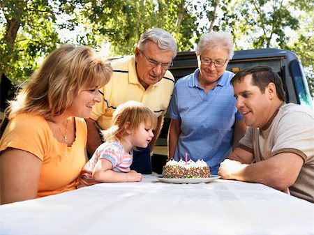 simsearch:400-05314669,k - Three generation Caucasian family seated at picnic table celebrating female childs birthday with cake. Photographie de stock - Aubaine LD & Abonnement, Code: 400-03937827