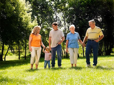 simsearch:400-05314669,k - Three generation Caucasian family holding hands walking across grass in park smiling. Photographie de stock - Aubaine LD & Abonnement, Code: 400-03937823