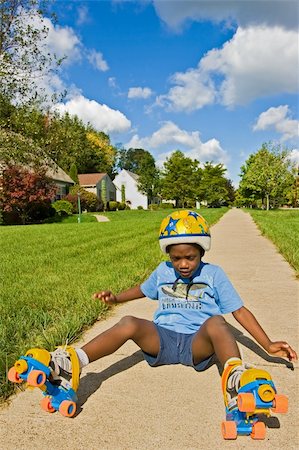 A young African American boy falls down while roller skating - wearing skates and a helmet. Foto de stock - Royalty-Free Super Valor e Assinatura, Número: 400-03938694