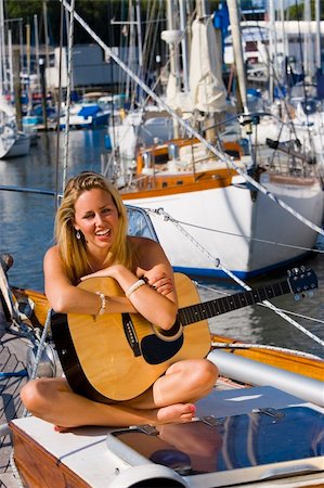 simsearch:400-04082089,k - A gorgeous young blond woman sitting on the deck of a yacht resting on her guitar and gloriously illuminated by golden evening sunshine Stock Photo - Budget Royalty-Free & Subscription, Code: 400-03931630