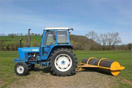 simsearch:400-07429043,k - Blue and white deisel tractor with a yellow roller attached to the rear, standing idle on farmland in rural countryside in spring. Foto de stock - Royalty-Free Super Valor e Assinatura, Número: 400-03931945