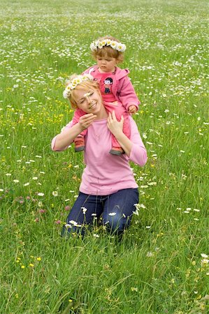 simsearch:400-06087517,k - Baby girl sitting on her mothers neck wearing daisy wreath and picking more daisies on a meadow full of flowers Stock Photo - Budget Royalty-Free & Subscription, Code: 400-03933760