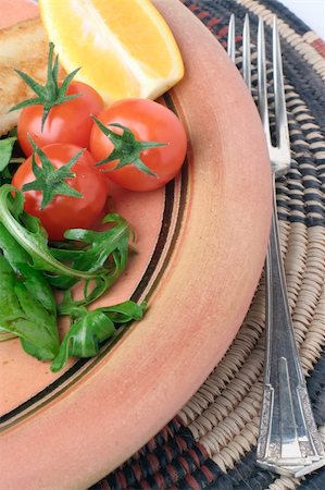 A glazed stoneware plate with Salad and fork on an African woven table mat. Stockbilder - Microstock & Abonnement, Bildnummer: 400-03946946