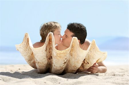 simsearch:400-03942507,k - Romantic couple on the beach kissing behind the seashell Fotografie stock - Microstock e Abbonamento, Codice: 400-03941328